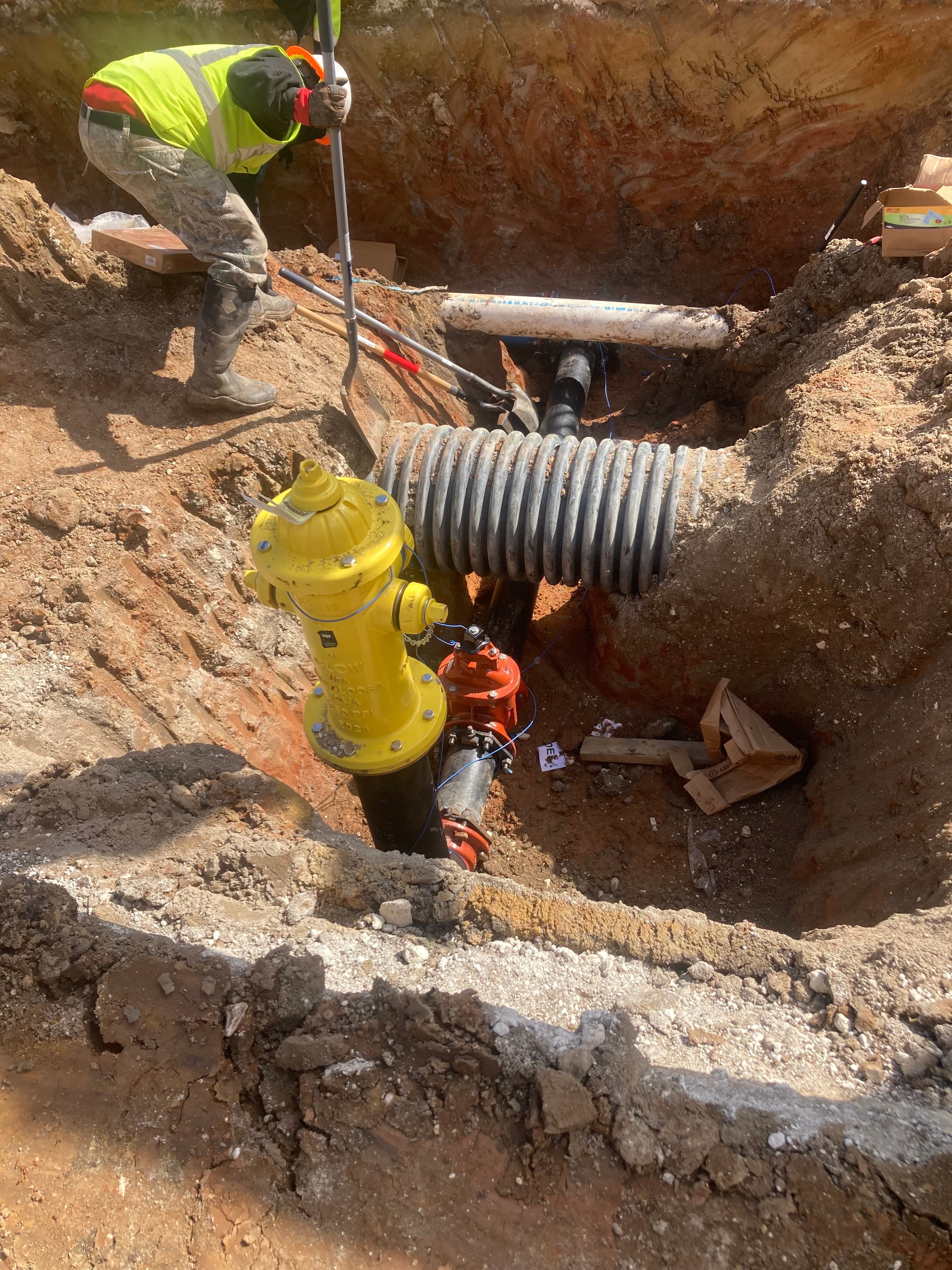 Dunn crew member in high-visibility gear setting a fire hydrant assembly in an excavation